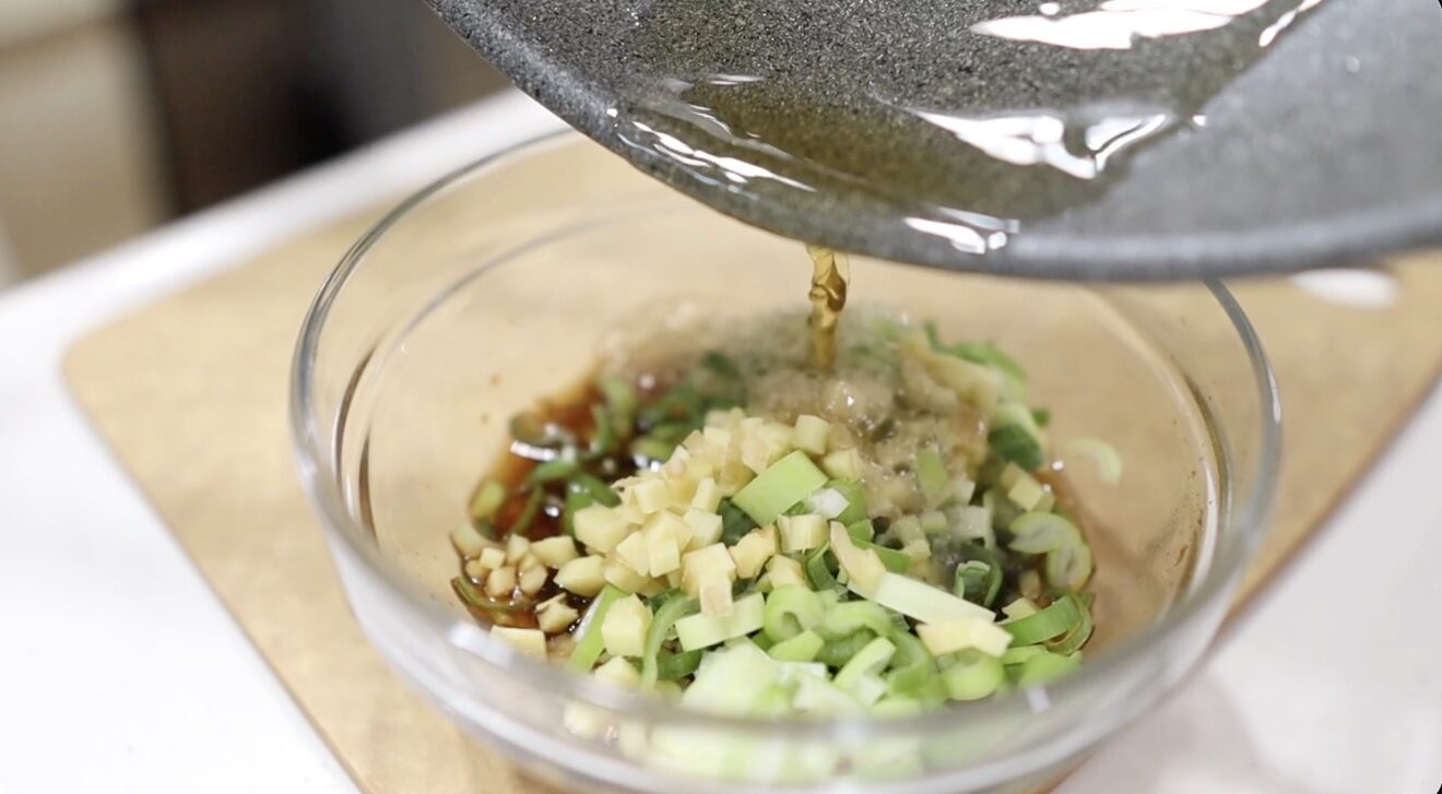 熱いごま油を薬味にかけてよだれ鶏のタレを仕上げる